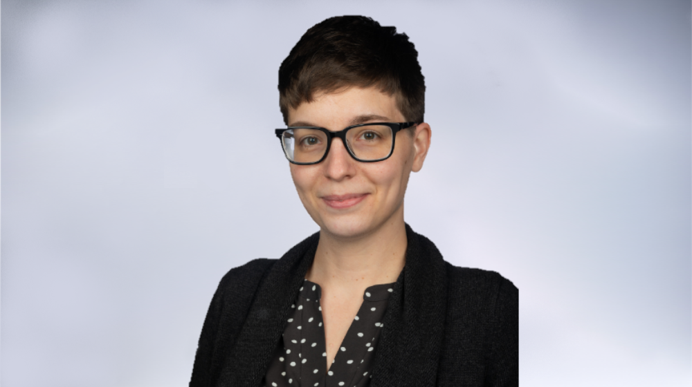Professional headshot of a person with short hair and glasses, smiling against a light background